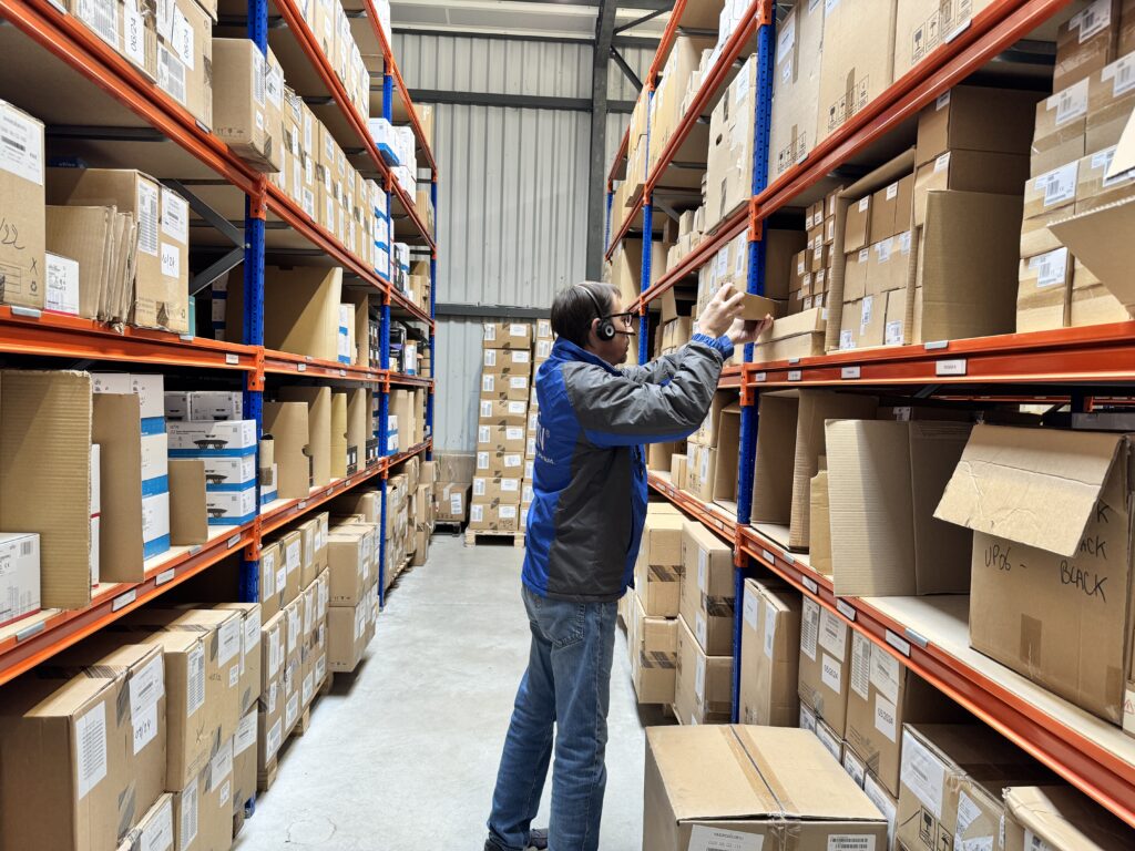 Employé vérifiant des stocks de vidéoprotection dans un entrepôt avec des étagères remplies de cartons